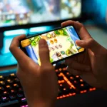 Χέρια παίζουν παιχνίδι σε smartphone, με φωτισμένο πληκτρολόγιο gaming στο…