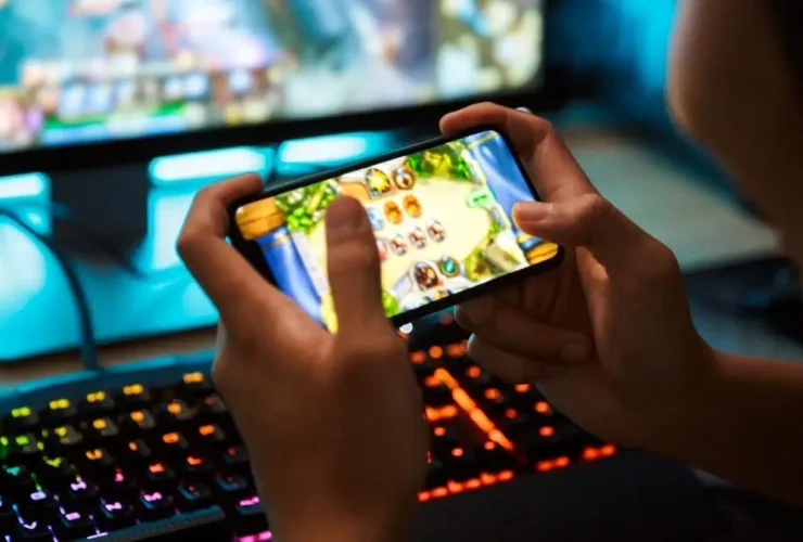 Χέρια παίζουν παιχνίδι σε smartphone, με φωτισμένο πληκτρολόγιο gaming στο…